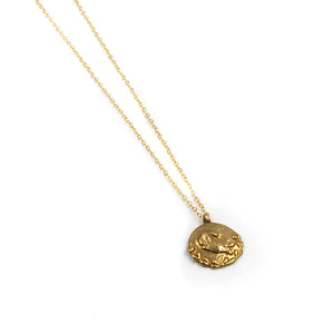Sleeping bunny carved into a brass pendant and hung on a gold fill chain on a white background