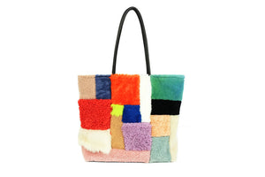 Multi-colored and multi-shaped sherling tote with black leather straps on white background